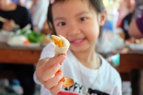 young child at crab feed holding up crab leg in front of the camera 